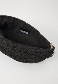 Borsa nera in crochet con un esterno testurizzato, dotata di una cerniera dorata e di un rivestimento in tessuto nero. L'etichetta interna reca la scritta "PIECES."