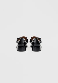 Chaussures en cuir verni noir avec un petit talon bloc, ornées d'un nœud décoratif à l'arrière et d'une texture lisse.