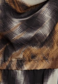 Tissu à motifs marron, noir et crème avec une texture douce ; présente un motif à carreaux flou et une section froncée à l'ourlet.