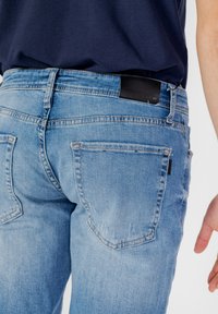 Jeans de mezclilla azul claro con un acabado desgastado, que cuentan con dos bolsillos traseros, costuras en contraste y una etiqueta de cuero negro en la cintura.