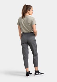 Grijze cropped pants met oranje stikdetails, gecombineerd met een beige t-shirt en zwarte high-top sneakers. De pasvorm is ontspannen.