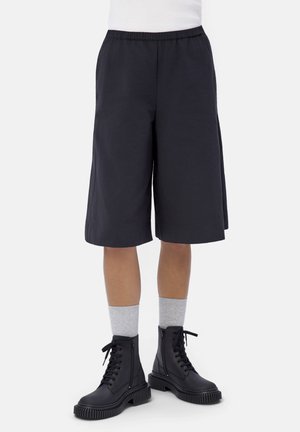 Personne portant un short large noir jusqu'aux genoux, des chaussettes grises claires et des bottines noires à lacets avec semelles épaisses.