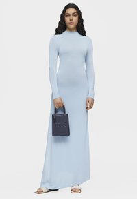 Abito lungo azzurro chiaro a maniche lunghe con silhouette aderente, tessuto testurizzato, indossato con una piccola borsa navy con logo in rilievo.