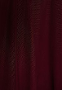Tissu rouge foncé à texture fine en maille avec des plis verticaux subtils créant des variations d'ombre sur la surface.
