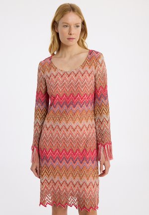 Robe en tricot avec un motif en zigzag dans des tons de rose, marron et bleu. Elle présente des manches longues avec des accents en franges et un col rond.