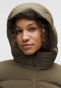 Opatentowana, pikowana kurtka z kapturem w kolorze oliwkowej zieleni, zapinana na zamek. Posiada wysoki kołnierz i fakturowaną tkaninę zapewniającą ciepło i komfort.