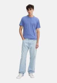 Camiseta de algodón azul claro con cuello redondo y logotipo en el pecho, combinada con jeans azul claros de corte suelto y zapatillas blancas.
