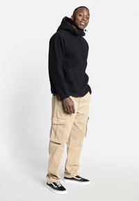 Hoodie zippé en polaire noir avec une capuche, comportant une poche avant. Assorti à un pantalon cargo beige et des baskets noires avec des accents blancs.