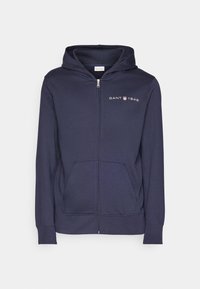 Felpa con zip di colore blu navy, realizzata in tessuto morbido, con tasca frontale a marsupio, polsini a costine e logo GANT 1949 sul lato sinistro del petto.