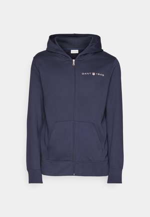 Navy blue zip-up hoodie made of soft fabric, featuring a front pouch pocket, ribbed cuffs, and GANT 1949 logo on the left chest.