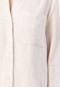 Beige linnen overhemd met knopen, een v-hals, een borstzak en een textuurstof die een losse pasvorm en een subtiel rustiek patroon heeft.