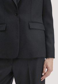 Zwarte op maat gemaakte blazer van textuurstof, met een enkele knoopsluiting en twee voorzakken, gecombineerd met bijpassende broek.