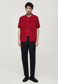 Rode T-shirt met korte mouwen en een patroon, gecombineerd met een rode T-shirt en zwarte broek. Zwarte schoenen maken de outfit compleet.