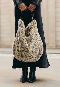 Sac à main en fausse fourrure crème à taches noires, doté d'un design décontracté et de poignées en cuir brun avec des anneaux dorés.