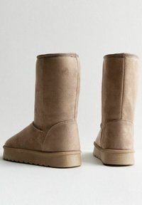 Beige mockasin höga stövlar med en platt, texturerad sula och en sömlös design. Har en rund tå och en enkel, hög siluett.
