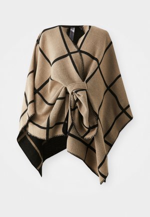 Poncho beige en tissu doux, présentant un grand motif de carreaux noirs, un centre noué et un ourlet frangé le long des bords.