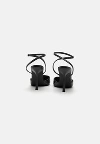 Sand�álias de salto alto pretas com um design elegante, apresentando tiras cruzadas nos tornozelos e um acabamento brilhante. Com bico aberto e salto agulha.