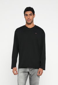 Juoda ilgomis rankovėmis palaidinė su apvalia iškirpte, subtiliomis siuvimo detalėmis ir mažu logotipu ant krūtinės. Pagaminta iš minkštos medžiagos.