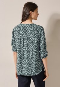 Blusa verde a stampa con vestibilità larga, dotata di scollatura rotonda e maniche lunghe arrotolate, realizzata in tessuto leggero.