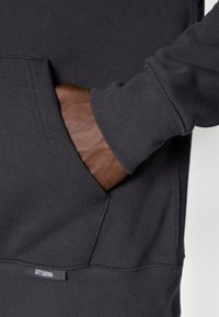 Felpa grigio scuro con tasca a marsupio e polsini a costine, con un piccolo etichetta "CITY EDITION" visibile all'orlo. Materiale morbido in misto cotone.