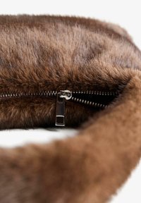 Hnědá kožená kabelka s zipovým uzávěrem se stříbrným kovovým táhlem, měkká textura a kulatý tvar s plyšovým vzhledem.