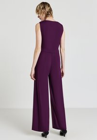 Lila ärmelloser Jumpsuit mit tailliertem Oberteil, weitem Bein und seitlichen Taschen, aus glattem Stoff, von hinten präsentiert.