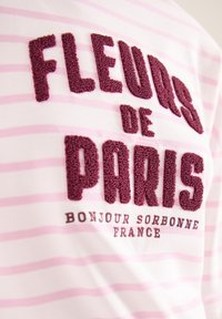 Teksturerede bourgognefarvede bogstaver, der læser "FLEURS DE PARIS" på et pink og hvidstribet stof med mindre tekst "BONJOUR SORBONNE FRANCE".