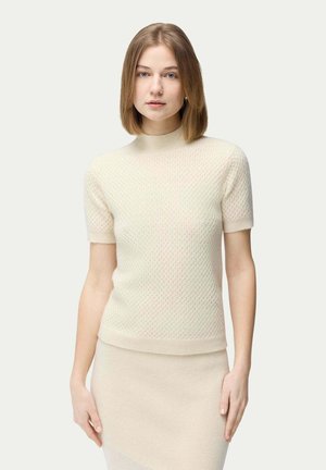 Pull en tricot beige clair avec des manches courtes, un col haut et un motif texturé. Associé à une jupe beige clair assortie.