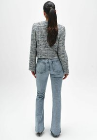 TEXTUUR, GEKROPEN TWEED JAS IN TINTEN VAN BLAUW EN WIT, GEPAARD MET LICHTBLAUWE FLARE JEANS MET ACHTERZAKKEN EN EEN RUWE RAND.