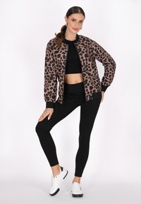 Giacca bomber con stampa leopardata in marrone e nero, abbinata a un crop top nero e leggings neri a vita alta. Sneakers bianche con dettagli neri.