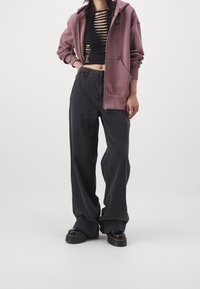 Svarta vida byxor med hög midja, kombinerat med en svart kort topp med horisontella skärningar. En lös ljuslila zip-up hoodie fulländar looken.