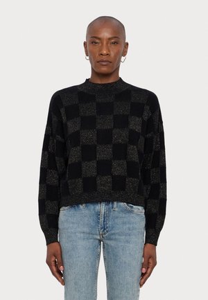Pulover scurt, cu guler înalt, în carouri negre și aurii, cu mâneci lungi, având un model texturat de tricot. Poartă-l cu blugi de culoare albastru deschis.