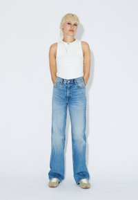 White sleeveless top paired with light blue, high-waisted, wide-leg jeans. The jeans feature a classic five-pocket design and subtle fading.