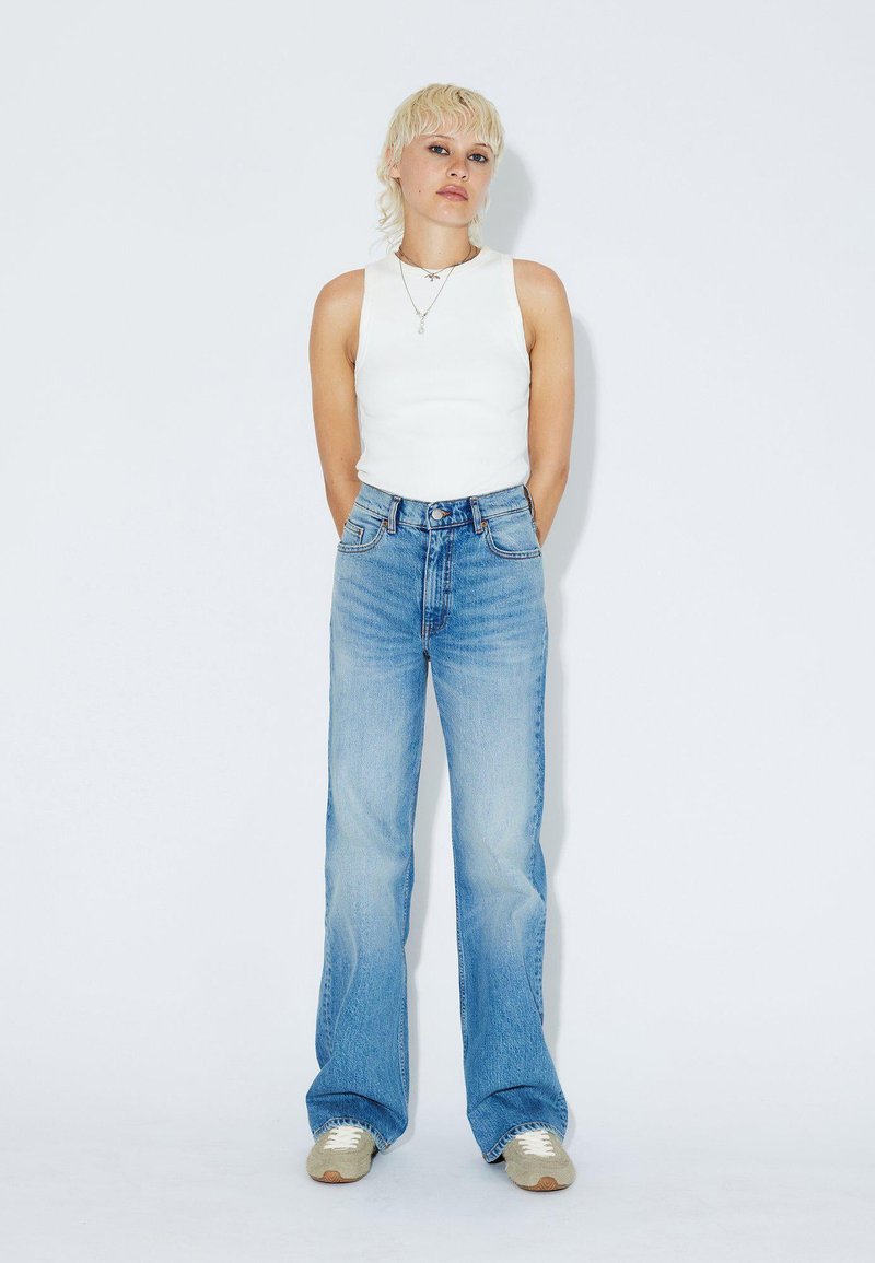 White sleeveless top paired with light blue, high-waisted, wide-leg jeans. The jeans feature a classic five-pocket design and subtle fading.