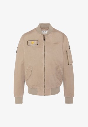 Veste bomber beige avec fermeture éclair avant, poignets et ourlet côtelés, deux poches avant, une poche zippée sur la manche, et des écussons brodés sur la poitrine et la manche.