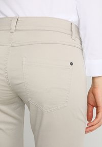 Svetle béžové kalhoty se slim fit střihem, detaily na zadních kapsách a jemným prošitím. Směs bavlny zajišťuje hladkou texturu.