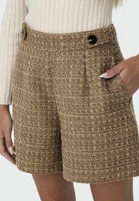 Shorts en tweed marron avec un motif texturé, taille haute, deux poches latérales et accents de boutons noirs. Idéaux pour une tenue décontractée.