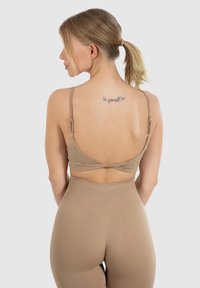 Beige sports-bh med justerbare stropper og krydsrygdesign, parret med højtaljede matchende leggings. Glat, elastisk tekstur.