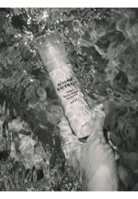 Main tenant une bouteille de Susanne Kaufmann Ectoin Barrier Repair Moisturiser SPF 50 immergée dans une eau ondulante.