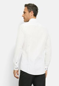 Weißes Langarmhemd mit Knopfmanschette, klassischem Kragen und einer glatten, leicht strukturierten Oberfläche. Sauberes Design, schlanker Schnitt.