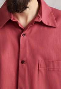 Korte mouw shirt in een gedempte rode kleur, voorzien van een puntige kraag, een borstzak en een knoopsluiting met donkere knopen. Gladde stofstructuur.