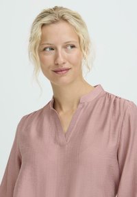 Helles rosa Bluse mit V-Ausschnitt, langen Ärmeln und strukturiertem Stoff. Verfügt über subtile Fältelungen an den Schultern für zusätzliche Details.