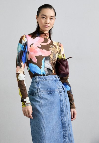 Μακρυμάνικη μπλούζα με πολύχρωμο λουλουδάτο σχέδιο σε καφέ φόντο, συνδυασμένη με ψηλόμεση ανοιχτό μπλε τζιν φούστα και μικρή μπορντώ τσάντα.