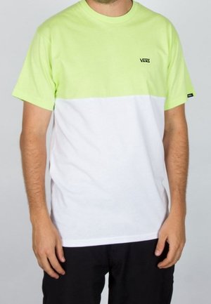 Mężczyzna noszący krótki t-shirt Vans z limonkową górną połową i białą dolną połową, w zestawieniu z czarnymi spodniami.