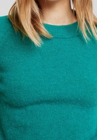 Tropfgrüner Strickpullover mit Rundhalsausschnitt und Raglanärmeln. Der Stoff wirkt weich und strukturiert und zeigt ein gemütliches Design.