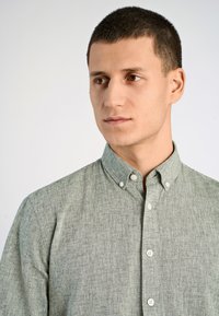 Jasnozielona koszula z rozpinanym kołnierzykiem, wykonana z teksturowanej tkaniny. Posiada tradycyjny kołnierz oraz białe guziki z przodu.