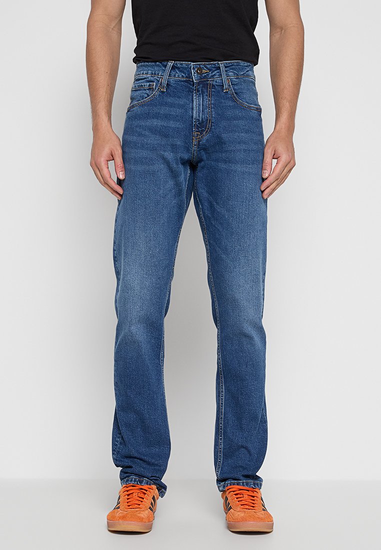 Blaue Denim-Jeans mit geradem Bein, ausgestattet mit fünf Taschen und dezenten Verwaschungen. Tragen mit orangen Sportschuhen.