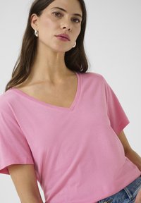 Rózsaszín pamut póló V-nyakkivágással, rövid ujjú és laza fazonnal. Simább textúra, egyszerű dizájn, minták vagy díszítések nélkül.