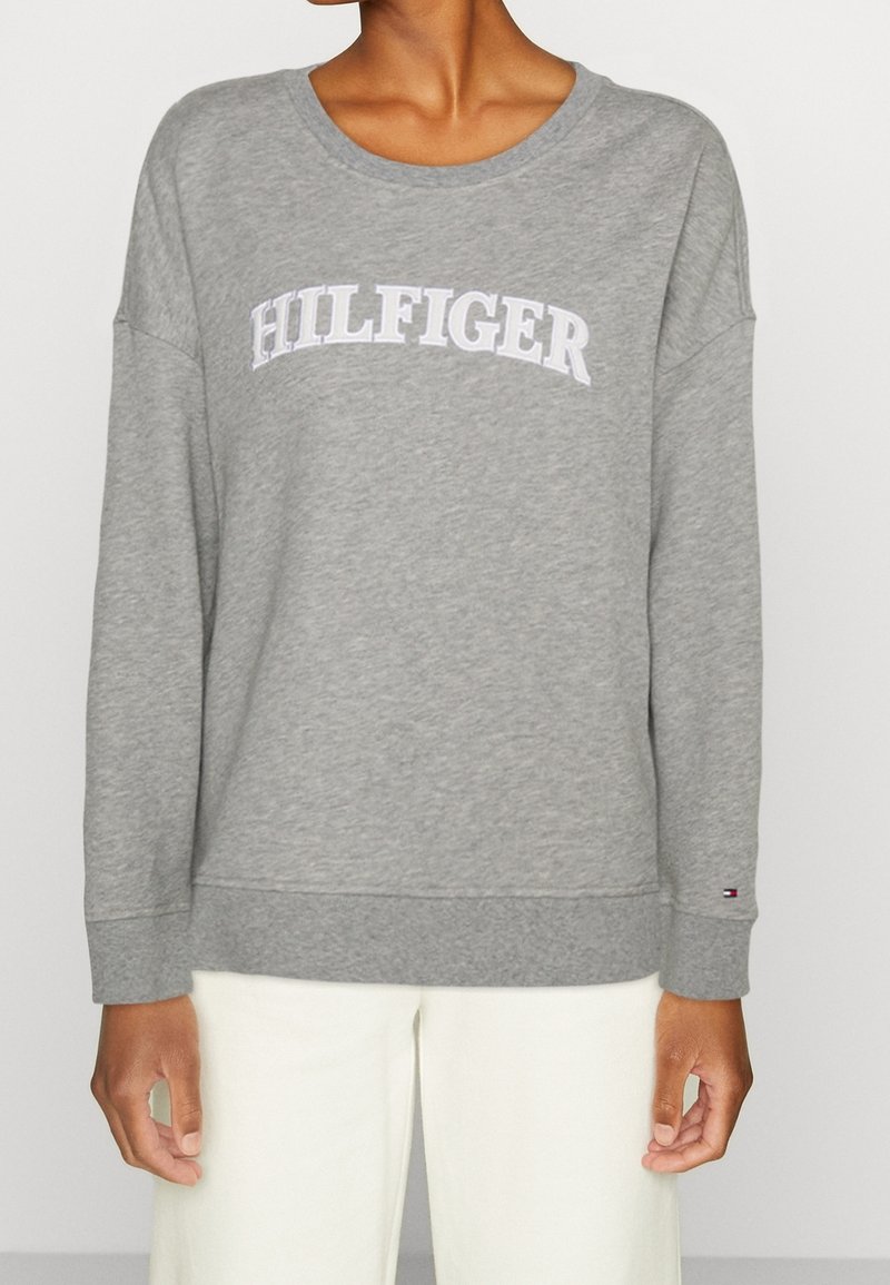 Felpa grigia realizzata in tessuto morbido, con scollo rotondo, maniche lunghe e grande logo bianco "HILFIGER" sul petto.