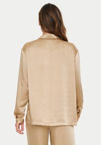 Satinbeige Bluse mit lockerem Schnitt, langen Ärmeln und Reverskragen. Verfügt über eine weiche Textur und dezenten Glanz. Rückansicht gezeigt.